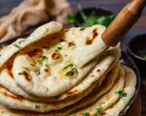 Frisch gebackenes Naan Brot wird mit Butter bestrichen und mit Kräutern bestreut.