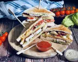 Ein gestapelter Club Sandwich mit Hühnchen, Speck, Ei und Tomaten, serviert mit Ketchup und Mayonnaise.