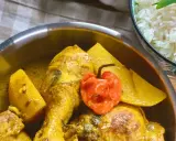 Colombo de poulet mit Kartoffeln und einer scharfen Chili, daneben eine Schüssel Reis.