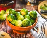 Frischer Rosenkohl in einer Schale, bereit, rosenkohl zuzubereiten wie Oma. Ein Holzlöffel liegt daneben.