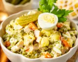 Ein cremiger Olivier Salat mit Erbsen, Karotten, Eiern und Gewürzgurken, garniert mit einer halben Eierschale und Petersilie.