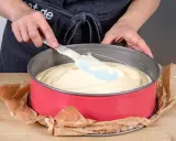 Hände verteilen den Teig für einen Joghurtkuchen mit 500 g Joghurt in einer roten Springform.