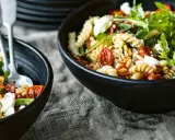 Zwei Schalen mit einem köstlichen nudelsalat mit getrockneten tomaten, garniert mit Rucola und Pinienkernen.