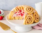Halbierte Erdbeer Charlotte auf einer Tortenplatte, gefüllt mit Erdbeercreme und frischen Erdbeeren, umhüllt von Biskuitrollen.