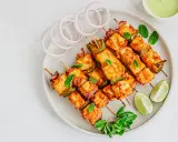 Saftiges paneer tikka auf Spießen, garniert mit Minze, Zwiebelringen und Limettenspalten.
