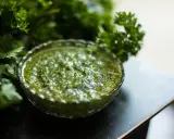 Frische Kräuter umgeben eine Schale mit leuchtend grünem Chimichurri. Was ist Chimichurri? Eine würzige argentinische Sauce aus Petersilie, Knoblauch und Essig.