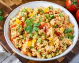 Frischer Couscous-Salat mit Tomaten, Paprika und Petersilie, garniert mit einem Petersilienblatt.