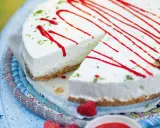 Cremiger Kuchen ohne Backen, dekoriert mit rotem Sirup und Limettenabrieb. Ein Stück ist bereits angeschnitten.