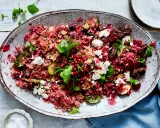 Rote Bete Bulgur Salat mit Granatapfelkernen, Feigen, Feta und frischen Kräutern auf einem ovalen Teller.