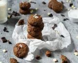 Gestapelte triple chocolate cookies mit Meersalzflocken, umgeben von Schokoladenstückchen und einem Glas Milch.