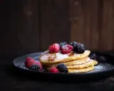 Ein Stapel fluffiger Pancakes, garniert mit frischen Beeren und Puderzucker. Ein perfektes pancakes rezept fluffig für jeden Anlass.