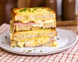 Ein gestapelter Croque Monsieur mit geschmolzenem Käse, Schinken und Schnittlauch auf einem Teller.