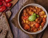 Herzhaftes Bauerntopf Rezept: Hackfleisch, Kartoffeln und Tomaten in einer Schüssel, garniert mit Basilikum. Dazu gibt es rustikales Brot.