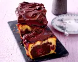 Saftiger Marmorkuchen mit Kirschen, überzogen mit dunkler Schokoladenglasur. Ein Stück ist bereits angeschnitten und zeigt die köstliche Marmorierung.