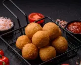 Goldbraune Arancini im Korb, bereit für ein köstliches arancini rezept. Dazu frische Tomaten, Salz und Dip.