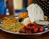 Vielfalt an indischen Gerichten auf einer Thali-Platte: Reis, Linsen, Curry und Papadum.