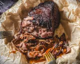 Saftiges pulled pork, zart zerfallen, mit BBQ-Sauce übergossen, auf Backpapier mit Gabeln.