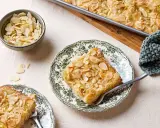 Ein Stück Butterkuchen mit Mandelblättchen auf einem Teller, daneben eine Schüssel mit Mandeln. Perfekt für ein Butterkuchen Rezept.