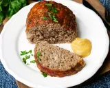 Saftiger hackbraten im ofen, auf einem Teller mit Senf und Petersilie garniert.