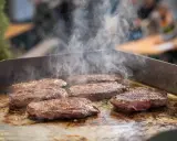 Mehrere saftige Steaks brutzeln auf einer heißen Platte. Dampf steigt auf und zeigt, wie man ein Steak richtig braten kann.