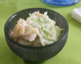 Ein cremiger Kartoffelsalat mit Joghurt und knackigem Gemüse, serviert in einer dunklen Schüssel auf einem hellgrünen Tischtuch.