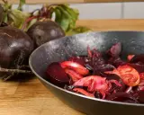 Rote Bete wird in einer Pfanne zubereitet, ein köstliches Hauptgericht. Frische Rote Bete liegt daneben.