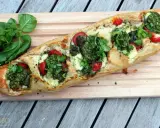 Ein knuspriges Baguette mit Pesto, geschmolzenem Käse und saftigen Tomaten, garniert mit frischem Basilikum.