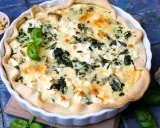 Herzhafte Quiche mit Spinat und Feta, garniert mit Pinienkernen und Basilikum.