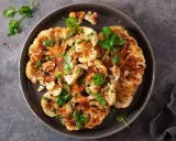 Geröstete blumenkohlscheiben im backofen, beträufelt mit grüner Soße und garniert mit Koriander.