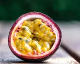 Eine aufgeschnittene Passionsfrucht mit saftigem, gelbem Fruchtfleisch und schwarzen Kernen liegt auf Holzplanken. Ein Genuss, diese Passionsfrucht zu essen!