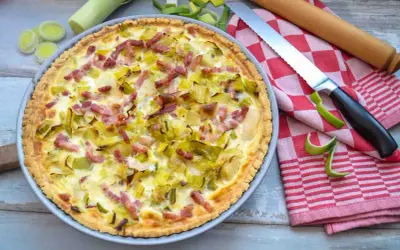 Herzhafte Quiche mit Lauch und Speck, perfekt für herzhafte Quiche Rezepte. Daneben liegen Lauch, ein Messer und ein Nudelholz.