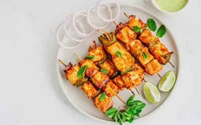Saftiges paneer tikka auf Spießen, garniert mit Minze, Zwiebelringen und Limettenspalten.