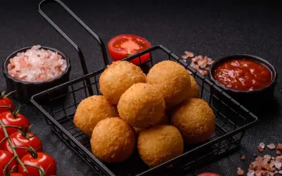 Goldbraune Arancini im Korb, bereit für ein köstliches arancini rezept. Dazu frische Tomaten, Salz und Dip.