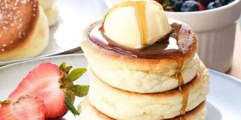 Fluffige japanische Pancakes mit einer Kugel Eis, Sirup und frischen Beeren.