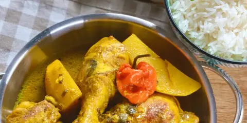 Colombo de poulet mit Kartoffeln und einer scharfen Chili, daneben eine Schüssel Reis.