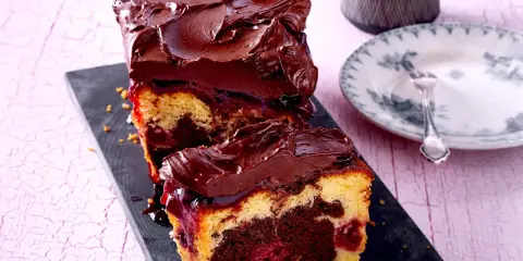 Saftiger Marmorkuchen mit Kirschen, überzogen mit dunkler Schokoladenglasur. Ein Stück ist bereits angeschnitten und zeigt die köstliche Marmorierung.