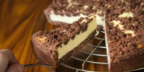 Ein Stück russischer Zupfkuchen wird aus dem Ganzen gehoben. Der Kuchen hat einen dunklen Boden, eine helle Füllung und eine krümelige Schokoladenstreusel-Decke.