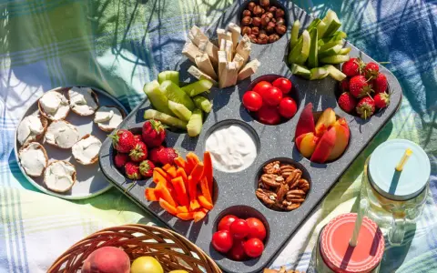Leckere Picknick-Snacks: Erdbeeren, Gurken, Karotten, Nüsse, Tomaten, Pfirsiche und Brotscheiben mit Frischkäse auf einer Decke.