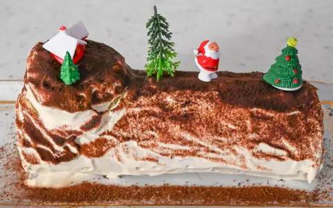 Eine festliche bûche de noël deutsch, verziert mit Weihnachtsmann, Bäumen und einem Haus.
