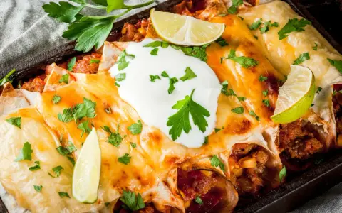 Herzhafte Enchiladas mit geschmolzenem Käse, saurer Sahne und Limettenspalten. Ein köstliches Enchiladas Rezept, das man probieren muss!