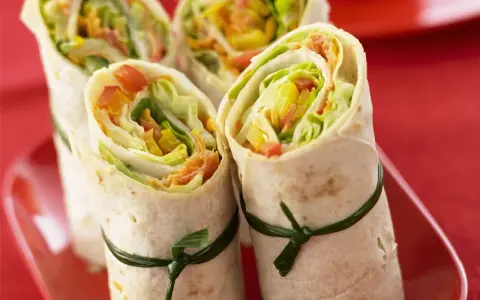 Vier gesunde wraps gefüllt mit knackigem Salat, Paprika und Karotten, kunstvoll mit grünen Bändern zusammengebunden.