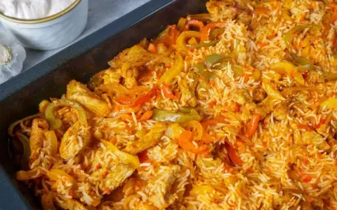 Herzhaftes One Pot Reis Ofen Gericht mit Hähnchenstreifen und bunten Paprikastreifen, serviert in einer schwarzen Auflaufform.