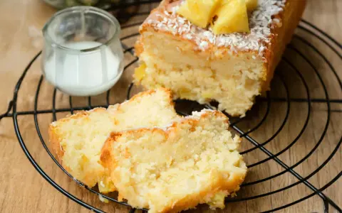 Saftiger ananas kokos kuchen mit frischer Ananas und Kokosraspeln, serviert auf einem Gitter mit einem Glas Milch.