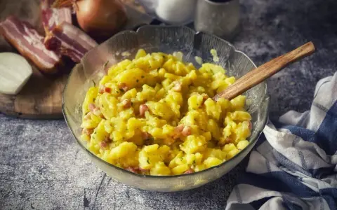 Schüssel mit warmem Kartoffelsalat, garniert mit Speck und Zwiebeln, bereit zum Servieren.