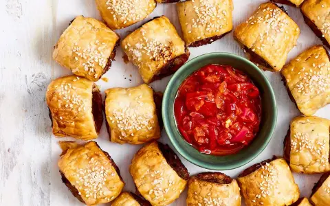 Goldbraune Würstchenschnecken mit Sesam, daneben eine Schale mit roter Chutney-Sauce. Perfekt, um schnelles Fingerfood am Vortag zuzubereiten.
