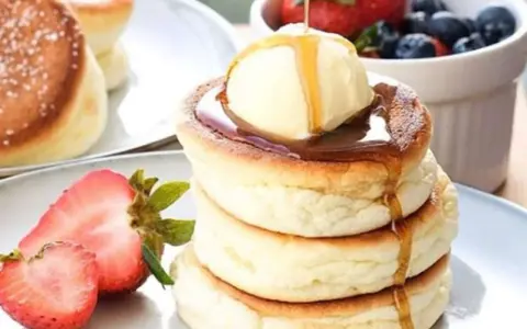 Fluffige japanische Pancakes mit einer Kugel Eis, Sirup und frischen Beeren.