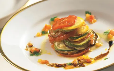 Ein kunstvoll geschichtetes Ratatouille-Rezept, inspiriert vom Film, mit Tomaten, Zucchini und Aubergine auf einem Teller mit goldenem Rand.