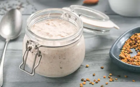Ein Glas cremiger Haferflocken-Pudding steht bereit, daneben eine Schale mit Pollen und ein Löffel.