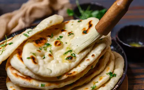 Frisch gebackenes Naan Brot wird mit Butter bestrichen und mit Kräutern bestreut.