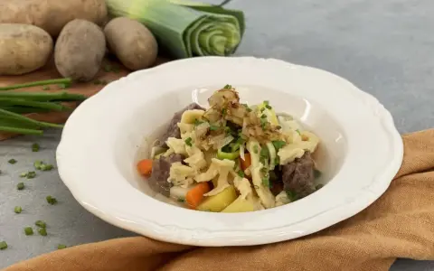 Herzhafter Gaisburger Marsch mit zarten Spätzle, Rindfleisch, Kartoffeln und Karotten, garniert mit Röstzwiebeln und Schnittlauch.